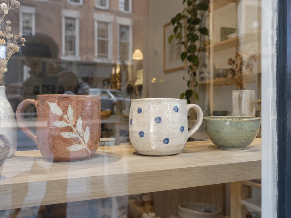 Handmade ceramic cups and bowls behind reflective shop glass